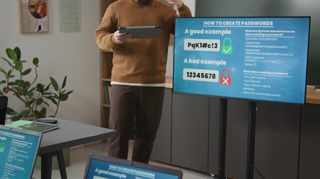 Tilt up shot of male teacher giving lecture on digital safety in computer class for seniors standing by board with safe password, focus flowing from students laptop, copy space