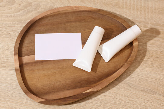 White blank crem tubes with white blank business card in a wooden tray. Beauty concept