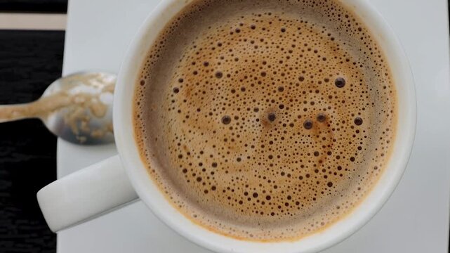 Top view of coffee crema and foam rotating in a white cup after stirring, creating swirling patterns and bubbles
