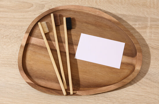 Eco bamboo toothbrushes with blank business card in wooden tray. Dental care