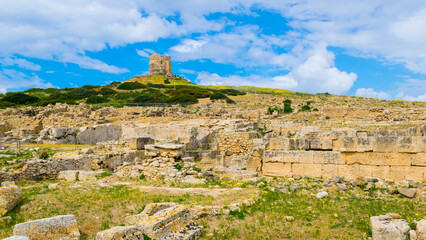 Fototapeta premium Sunny view of Tharros Archeological Area with Torre di San Giovanni di Sinis Tower in the background, Sardinia, Italy