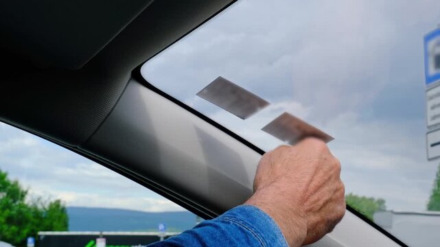 Unrecognizable man hands placing vignette sticker on car windshield from inside, preparing vehicle for road use, transport regulation and travel concept.