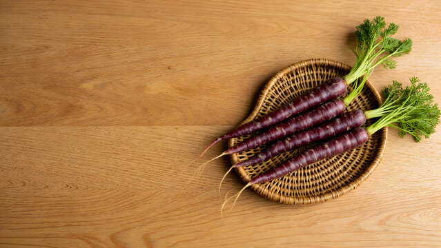 Fresh organic purple carrots in a wicker basket on a wooden table