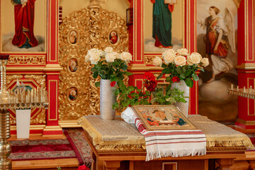 Obraz premium Religious icons and bouquets of white roses on a wooden table in an Orthodox church, sacred atmosphere, traditional worship, holy spirit.