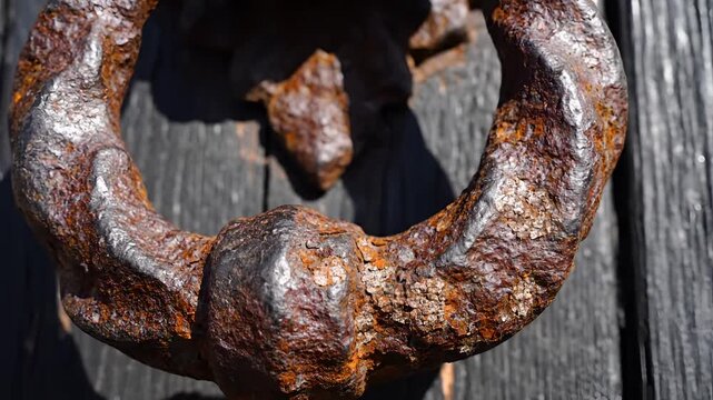 Closeup of a very old rusty ornate door knocker on a weathered wooden door.