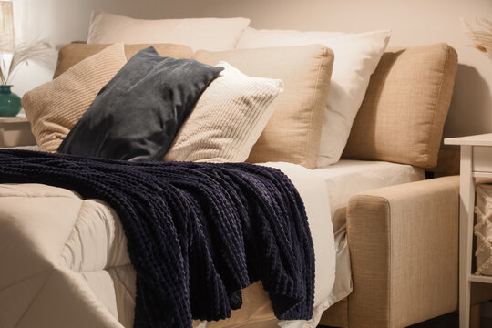 Bed with cozy blanket and soft pillows in stylish bedroom at night, closeup