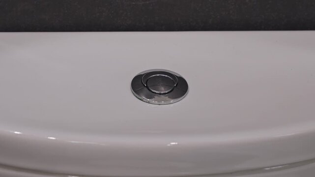 Person pressing pop-up drain stopper in bathroom sink