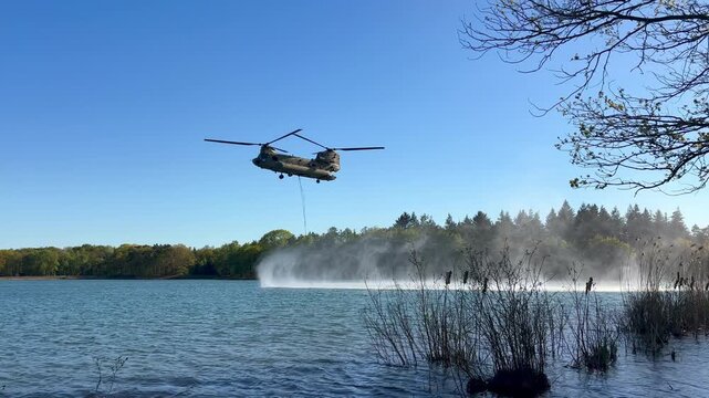 Transport helicopter of Dutch Royal Air Force carrying a water bucket for extinguishing wildfires in nature.