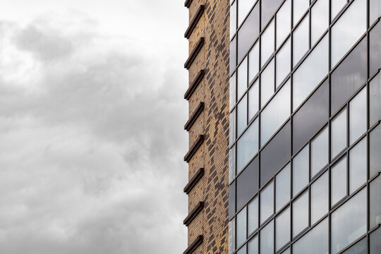 Brick meets glass windows in an urban architecture building facade with grid structure under sky and clouds offering calm editorial background copy space