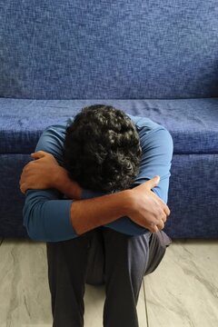 Depressed, exhausted, suicidal, hopeless or heartbroken young adult person sitting on floor hiding face. Sad, upset, crying, agony, grief, torment, despair, depression and mental breakdown concept.