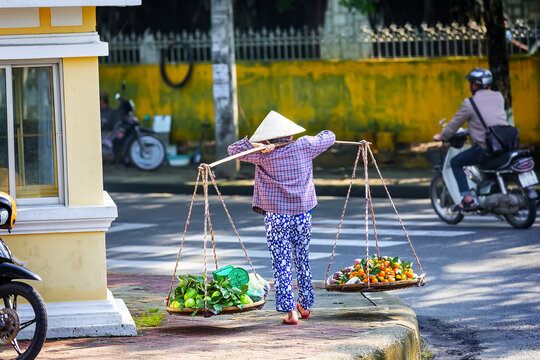 Traditional Vietnamese street vendor carrying baskets with tropical fruits in Ho Chi Minh City, Vietnam.
