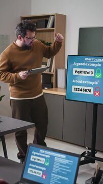 Vertical shot of male teacher leading computer literacy class for adults and giving lecture on scams and safety while standing by digital screen with password examples