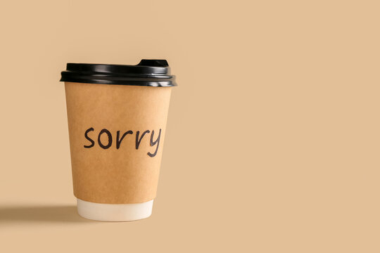 Paper cup of coffee with word SORRY on beige background