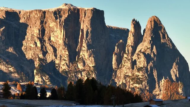 Majestic drone view of sunrise the view of Schlern (Sciliar) peak mountain in the Dolomites. Stunning alpine autumn colored forest all around, and yellow grass covered in morning white hoarfrost. Pict