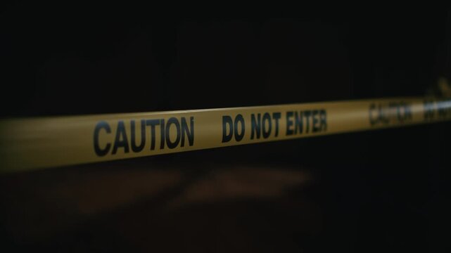 Yellow caution tape do not enter stretched across dangerous zone at night indicating restricted access and increased hazard in dark outdoor environment