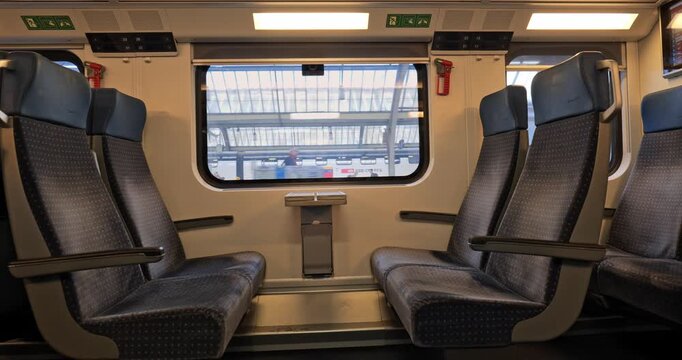 Empty seats inside passenger train slowly arriving at a large  train station platform in a European city. Wide angle, real time footage