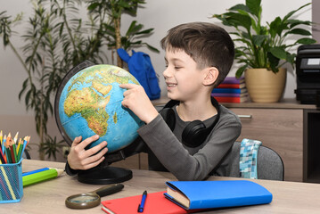 Happy school-age boy sitting at a table with a globe, exploring geography and studying at home. © nellas