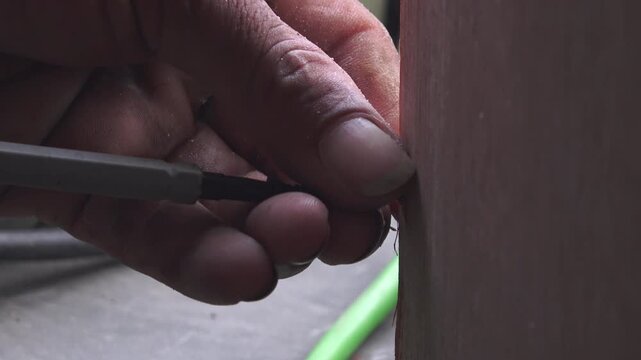 A worker's hands stabilize a power screwdriver to ensure a screw enters the plywood at the correct angle for a strong joint.