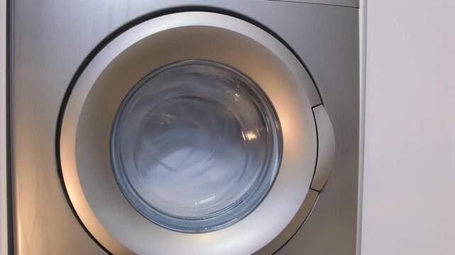 washing machine drum spinning close-up front view with high speed rotation during spin cycle, laundry process scene showing water extraction and fabric drying stage in modern home appliance