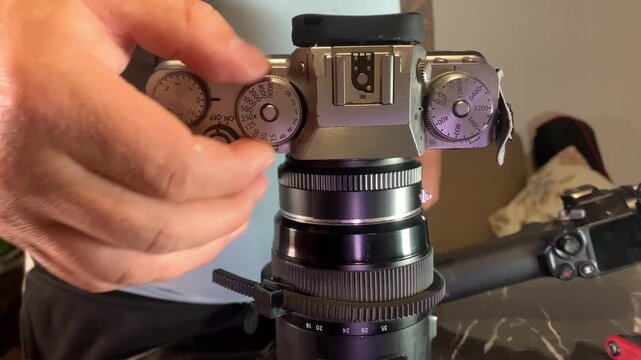 Hands turning shutter speed dial on camera close-up, adjusting exposure settings for motion control and light balance, precise manual control in photography workflow and image capture process