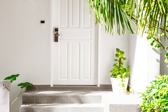 Entrance of house with white door, green tropical plants and foot wash faucet