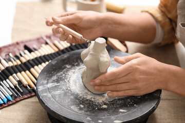 Fototapeta premium Hands of female sculptor with tool shaping clay figurine on pottery wheel in workshop