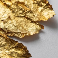 Fototapeta premium Close-up of irregular gold leaf fragments on white paper with dramatic metallic shine