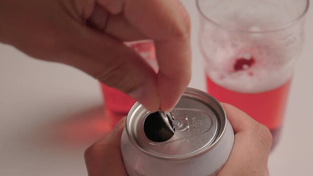 Closeup of can opening. Casual social scene with beverage and foam in background. Closeup shot of fingers lifting tab on aluminum can with drinks and foam in background