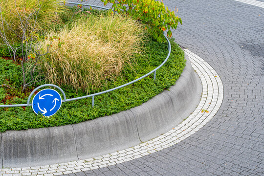 Roundabout sign at junction with island curb landscaping and roadway design provides urban traffic guidance for drivers in daylight outdoors