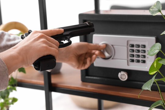 Woman with pistol opening safe on shelf at home, closeup