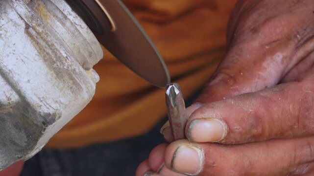 Close-up of a metal bit being held against a grinding disc, focusing on the precision of the sharpening process in a workshop.