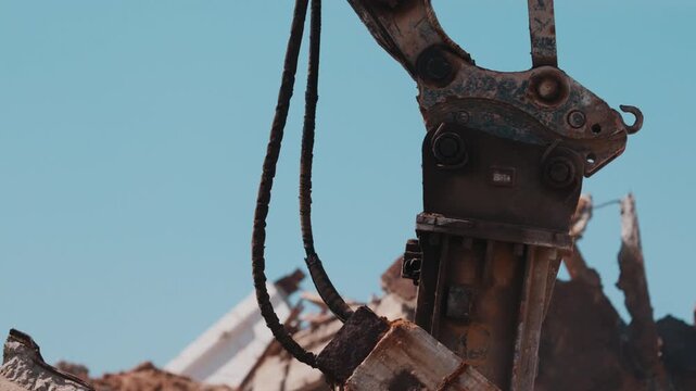Excavator hydraulic attachment crushing concrete debris during demolition close up