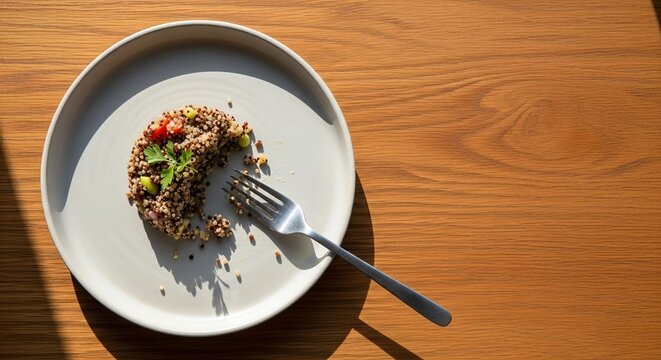 Small portion of healthy quinoa salad on light plate with metal fork on wooden table. Mindful eating concept for weight management and GLP 1 treatment. Conscious food choice and diet.