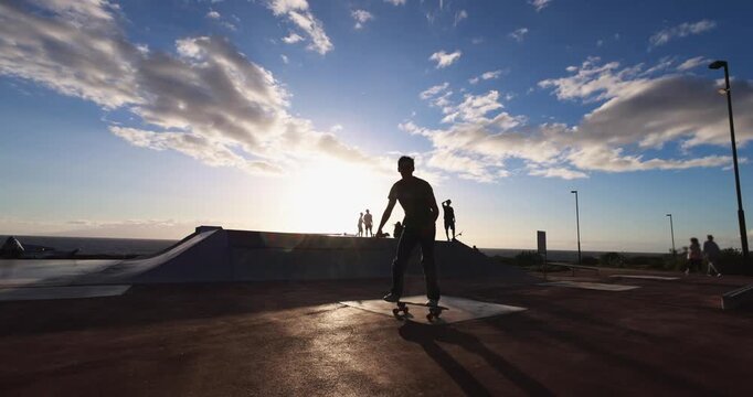 Young men having fun at skateboard park outdoor during sunset time - Summer lifestyle, people and extreme sport concept - UGC wide lens content