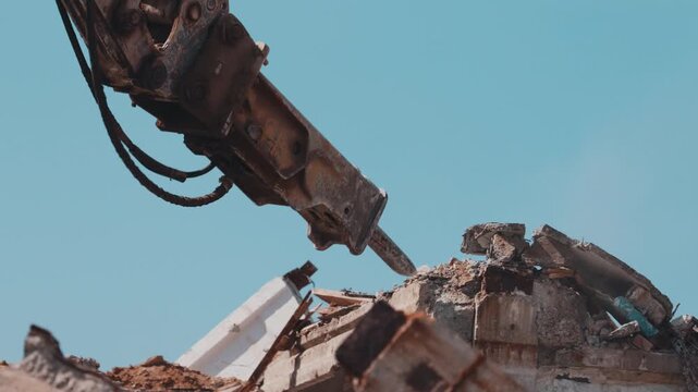 Excavator hydraulic hammer breaking concrete rubble on demolition site close up