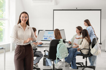 Obraz premium Female teacher with laptop and students studying at school computer lab
