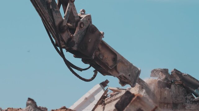 Hydraulic breaker on excavator demolishing concrete debris against sky