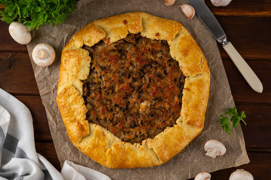 Savory galette or open pie with mushroom, onion and cheese on a dark wooden background. Rustic style. Top view.