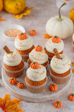 Pumpkin spice cupcakes decorated butter cream frosting, sugar sprinkles and mini sweet pumpkins on top. Thanksgiving or Halloween dessert.