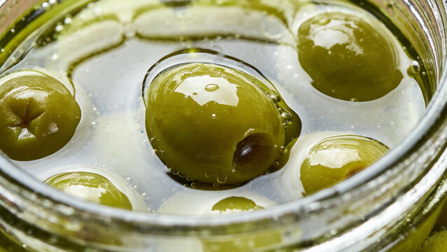Close up of green olives in brine inside a glass jar near an olive farm