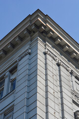 Obraz premium A low angle view of a grey classical building corner featuring decorative cornices and ionic order details against a clear blue sky