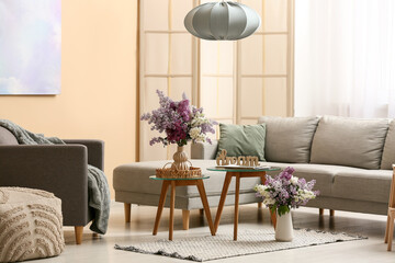 Interior of living room with sofa, armchair and lilac flowers in vases