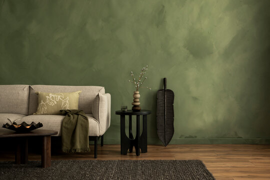 Stylish interior with copy space, design sofa, and personal accessories. Green limewash wall. 