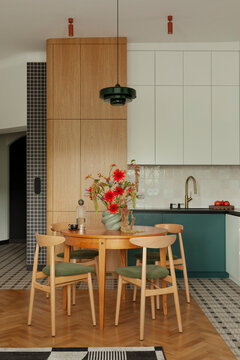 Modern kitchen and dining area with warm wood cabinetry, green seating, and vibrant red flowers create a cozy, stylish interior