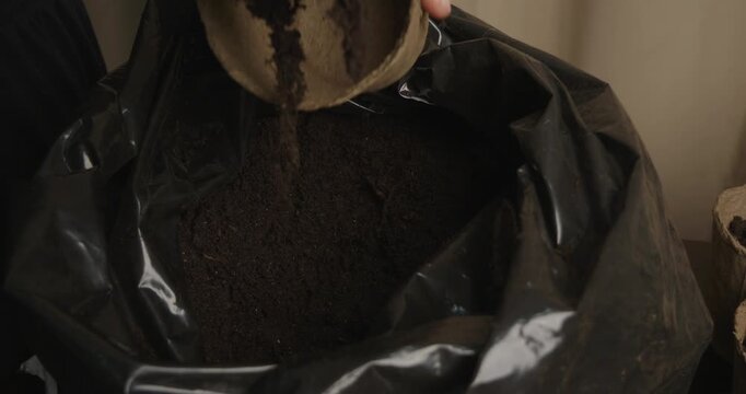 Close-up of a gardener's hands using a trowel to fill biodegradable peat pots with fresh soil, preparing them for transplanting tomato seedlings or other young plants for the spring season.
