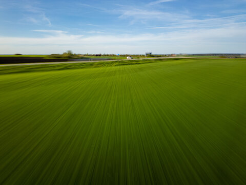 Dynamic motion blur aerial of green field and road with car