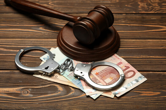 Handcuffs with judge's gavel and euro banknotes on wooden background, closeup