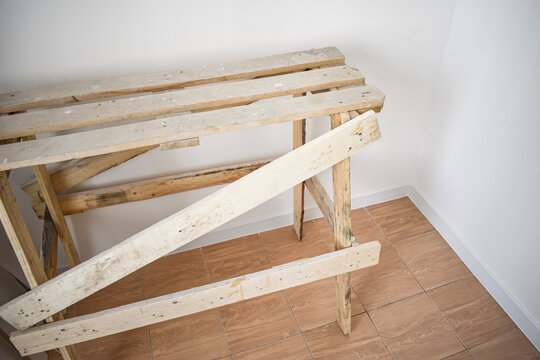 High angle shot of a wooden construction sawhorse assembly made of unpainted timber planks on a brown tiled floor in a room with white walls
