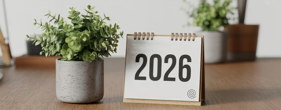 Desktop calendar showing the year 2026 next to a small potted green plant on a wooden table