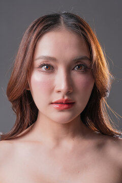 Extreme close-up beauty portrait of Asian woman with glowing skin and brown eyes, professional makeup and skincare concept on grey background